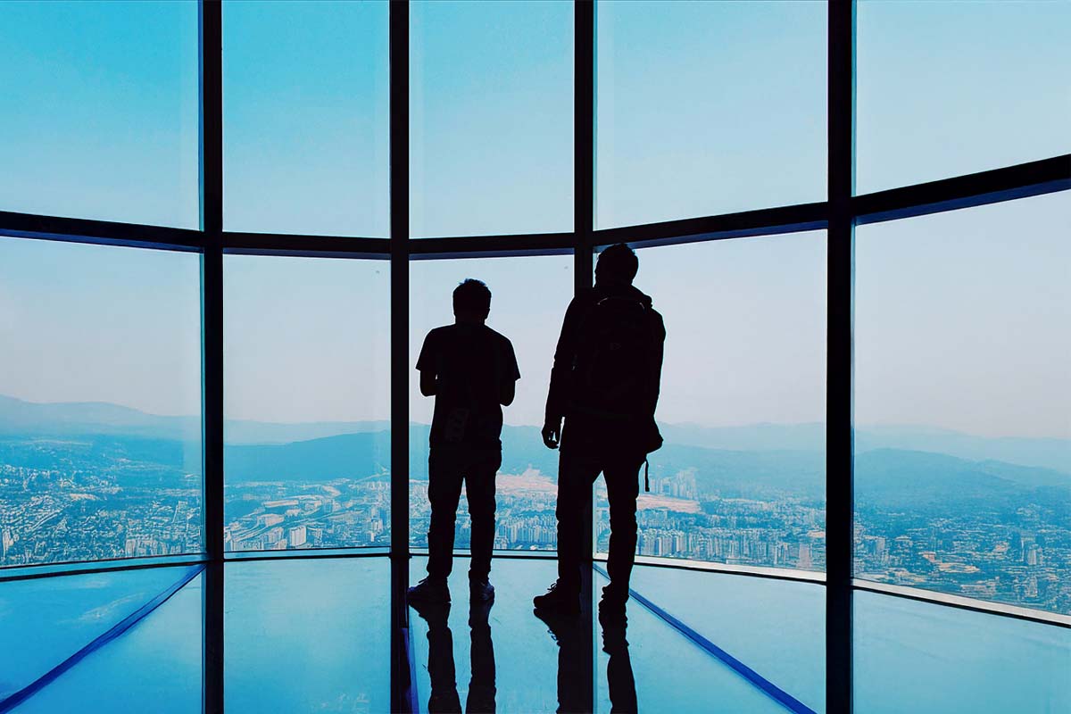Two people looking out over a city skyline from a high glass observation deck.