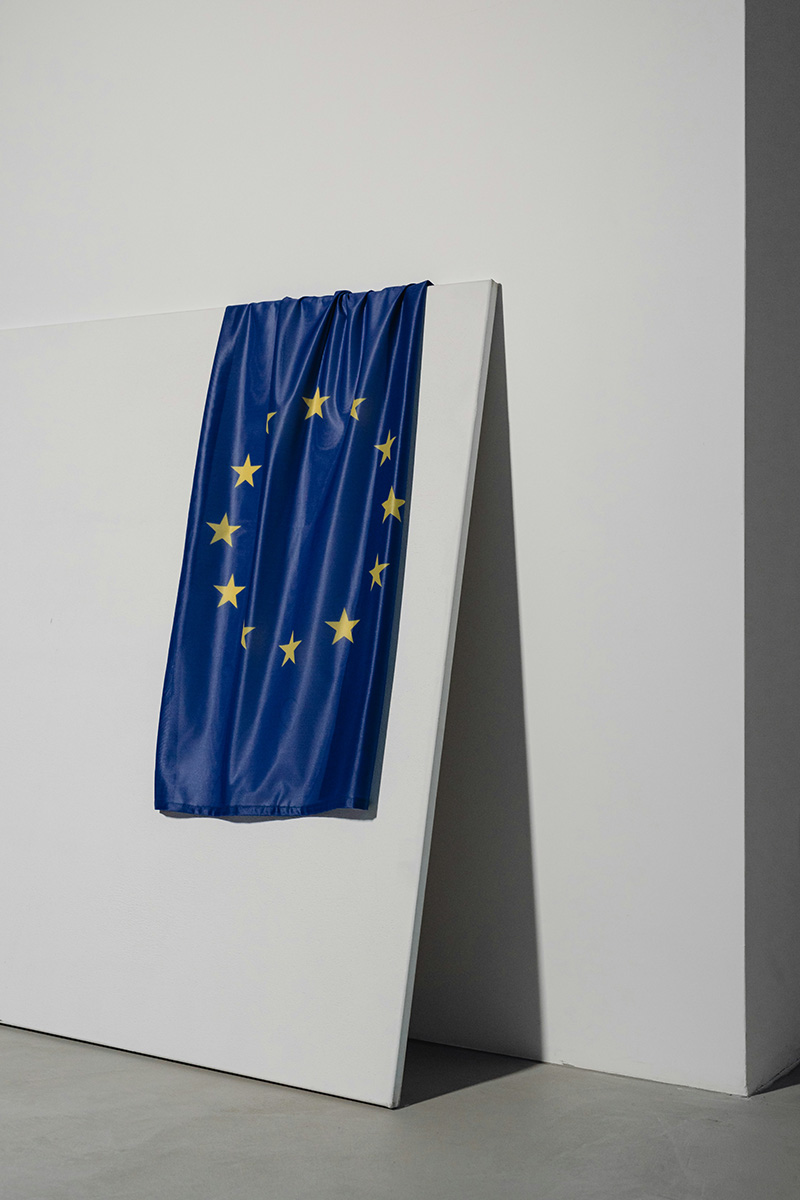 Stockimage of a European flag, draped over a wooden stand, agianst a white wall.